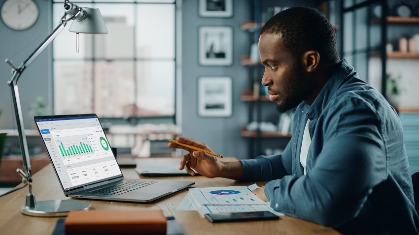 Handsome Black African American Specialist Working on Laptop Computer in Creative Home Living Room. Freelance Male is Doing Market Analysis and Creates Report with Charts for Clients and Employer.