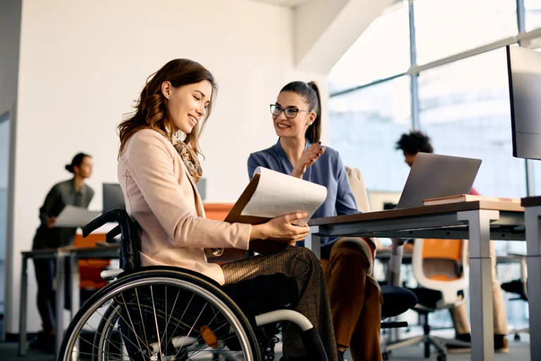 Employee in wheelchair at desk in conversation with colleague