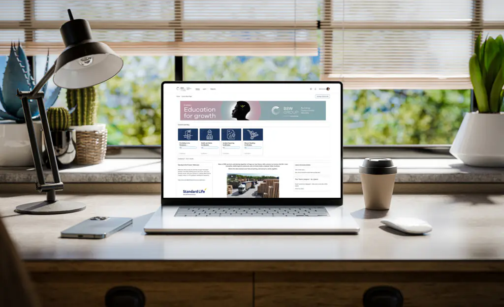 A laptop with a Totara LMS screen from BSW sits on on a stylish wooden desk within a loft-style interior, with green spaces in the background visible through the window - 3d render